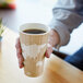 A person holding an Eco-Products World Art insulated paper hot cup with coffee.