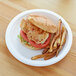 A chicken sandwich with tomato and lettuce on an Eco-Products white compostable sugarcane plate.