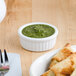 A plate of food with a Tuxton fluted white porcelain ramekin filled with green sauce and a fork.