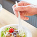 A hand holding an Eco-Products white compostable plastic fork over a bowl of salad.