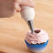 A hand using an Ateco closed star piping tip and pastry bag to pipe pink frosting on a cupcake.
