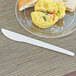 A plate of food with a sandwich and a white compostable plastic knife on it.