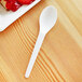 A white Eco-Products compostable plastic spoon on a wood surface.