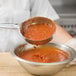 A person using a Vollrath Orange Solid Round Spoodle to pour red sauce into a bowl.