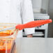 A person in a white coat uses a Vollrath Jacob's Pride orange spoodle to serve red sauce.