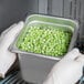 A person in white gloves holding a Choice stainless steel steam table pan filled with peas.