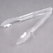 A clear plastic tongs with handles on a gray surface.