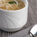 A white Libbey porcelain bouillon cup filled with soup and noodles.