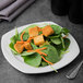 A plate of spinach salad with tofu cubes and carrots.