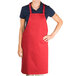 A woman wearing a red Chef Revival bib apron posing in a professional kitchen.