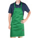 A man wearing a Kelly green Chef Revival apron with his hands on his hips.