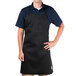 A man wearing a black Chef Revival bib apron with 1 pocket in a professional kitchen.