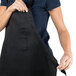 A woman holding a black Chef Revival bib apron with a pocket.