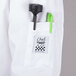 A white Chef Revival long sleeve chef jacket with a pocket holding a green pen and a green pen holder.