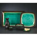 A black bowl with a green rim on a plate with other Libbey Hakone dinnerware.