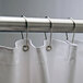 A white shower curtain with Bobrick stainless steel hooks hanging on a rod.