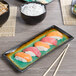 A Libbey stoneware platter with sushi and chopsticks on a table.
