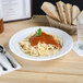 A Tuxton pasta bowl filled with spaghetti and sauce, with a slice of bread on the table.