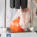 A person in gloves using a Vollrath Redco 3.5 fruit and vegetable corer to cut a tomato.