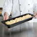 A chef holding a GET black melamine food pan filled with macaroni and cheese.