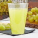 A Fineline clear hard plastic tumbler filled with yellow liquid on a table with grapes.
