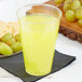 A Fineline Savvi Serve tall clear plastic tumbler filled with yellow liquid sitting on a table with grapes and crackers.