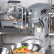 A silver mixer with a bowl of colorful peppers and a machine attachment.