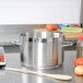 A Vollrath stainless steel sauce pot on a counter with a wooden spoon next to it.