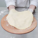 A person using an American Metalcraft round pizza peel to make dough on a wooden board.