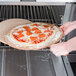A person using an American Metalcraft pizza peel to remove a pizza from an oven.