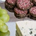 A Vollrath metal catering tray with cheese, salami, and meat on it, with a bunch of grapes.