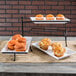 An American Metalcraft three-tier rectangular display stand with melamine platters holding trays of muffins on a table.