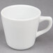 A 7.5 oz. bright white porcelain coffee cup with a handle on a gray surface.