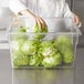 A chef putting lettuce in a Rubbermaid clear polycarbonate food storage container.