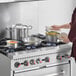 A woman cooking with Vollrath stainless steel pots and pans on a stove.