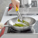 A person cooking asparagus in a Vollrath stainless steel pan on a stove.