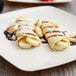 A plate of crepes with bananas and chocolate drizzled on top on a table.
