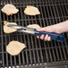 A person using Vollrath stainless steel tongs to grill meat.