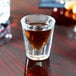 An Anchor Hocking shot glass filled with brown liquor on a table in a bar.