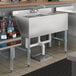A Regency stainless steel underbar sink with three compartments and a shelf of bottles.