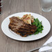 A Reserve by Libbey Aluma White Porcelain plate with a steak and green beans on it on a table.