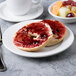 A bagel with jam on a Libbey Aluma white porcelain plate next to a bowl of fruit.