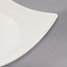 A Libbey ivory porcelain coupe plate with a curved edge on a gray surface.