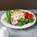 A white Aluma Reserve porcelain plate with a salad of chicken and vegetables.