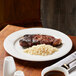 A Reserve by Libbey Aluma White Porcelain plate with steak and rice on a table.