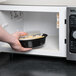 A hand placing a Pactiv Newspring VERSAtainer oval container of food in a microwave.