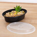 A Pactiv black plastic VERSAtainer oval microwavable container with rice and vegetables.