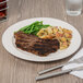 A Libbey Frama ivory porcelain plate with steak, potatoes, and green beans.