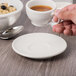 A hand holding a Libbey ivory porcelain small saucer with a cup of coffee.