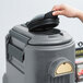 A hand putting a lid on a grey Cambro insulated beverage dispenser.